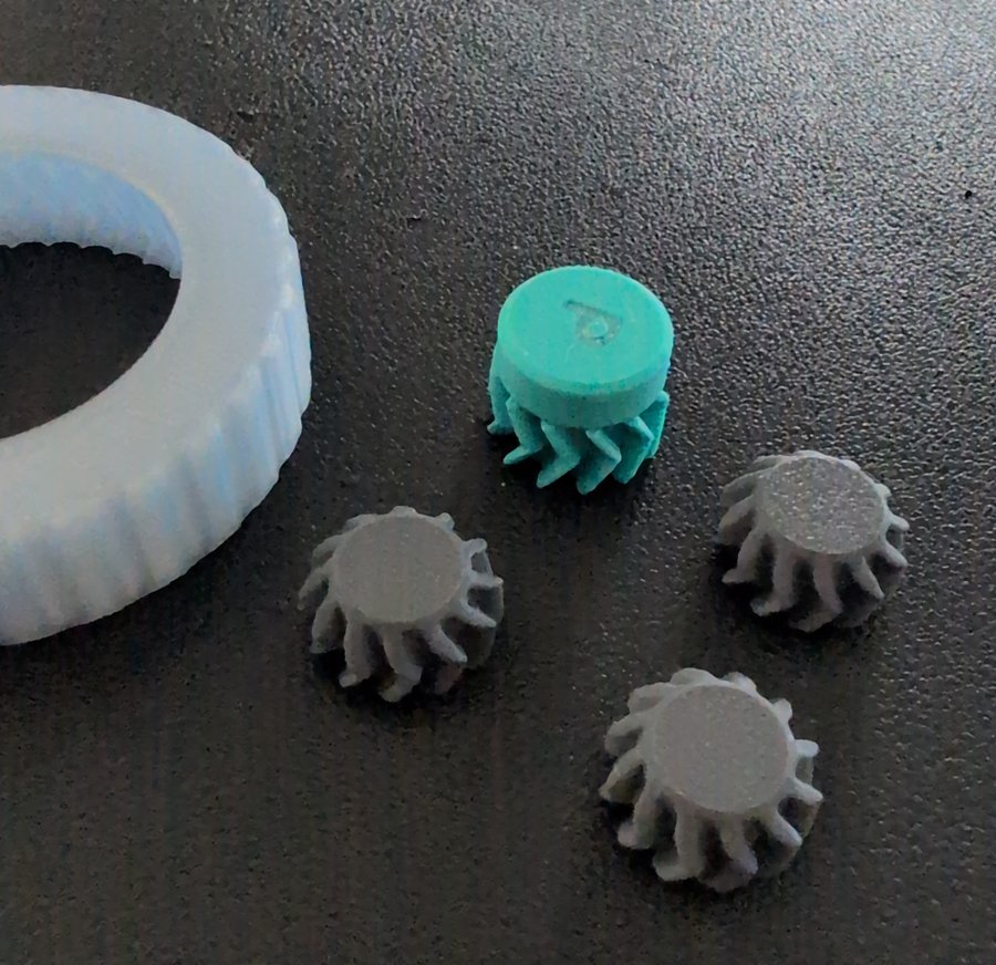 Photo of attempt 8 in pieces: the clear ring, the teal sun with its P cap and herringbone teeth, and three grey herringbone planet gears